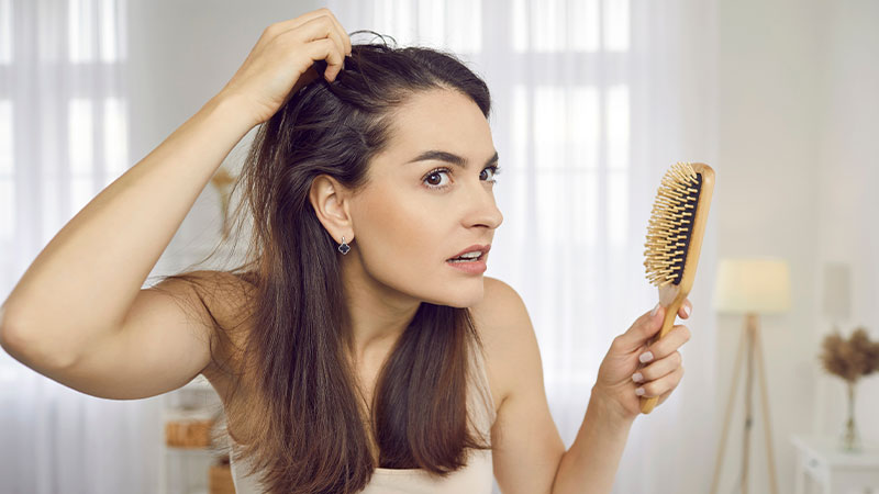 donna con spazzola in mano si guarda i capelli